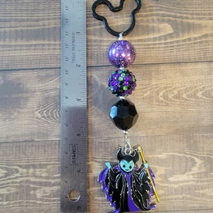 May include: A black Mickey Mouse-shaped keychain with a beaded design. The keychain features a purple glitter bead, a green and black rhinestone bead, a black faceted bead, and a Maleficent charm. The charm is approximately 2 inches in length.