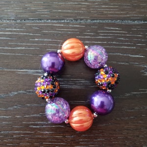 May include: A purple and orange chunky bead bracelet with a pumpkin design. The bracelet is made of large, colorful beads.