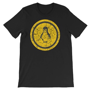 May include: Black t-shirt featuring a yellow circle with a distressed, worn look. Inside the circle is a black penguin graphic.