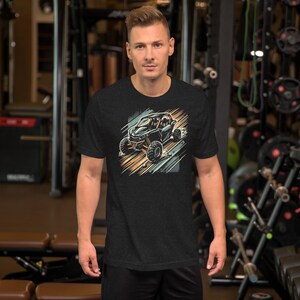 Könnte beinhalten: Ein schwarzes T-Shirt mit einem Aufdruck eines schwarzen Geländewagens, der auf einer Schotterpiste fährt. Das Fahrzeug hat eine gelbe und orangefarbene Farbgebung und ist von einem blauen und orangefarbenen Hintergrund umgeben.