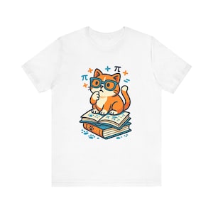 Può includere: Una t-shirt bianca con la grafica di un gatto arancione che indossa occhiali blu, seduto su una pila di due libri. Il gatto è circondato da simboli matematici tra cui il simbolo pi greco, segni più e un segno di uguale, con impronte sotto.