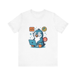 May include: A white t-shirt featuring a graphic of a blue penguin wearing black glasses and typing on a laptop. The design includes orange feet and beak, with circular icons representing code, the Python logo, and the Java logo surrounding it.