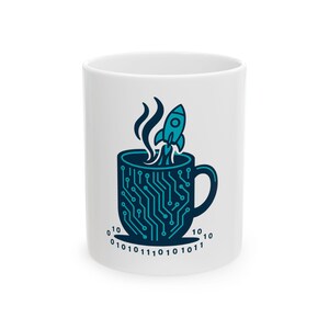 May include: A white ceramic mug featuring a dark blue graphic of a coffee cup with a circuit board pattern. A small rocket ship launches from the top of the cup, emitting steam. The base of the mug is surrounded by binary code digits 0 and 1.
