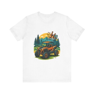Może przedstawiać: Biały t-shirt z grafiką przedstawiającą pomarańczowy pojazd terenowy przewożący lodówkę wypełnioną brązowymi szklanymi butelkami. Tło przedstawia stylizowany krajobraz leśny z zielonymi sosnami, pagórkami i żółtym słońcem na horyzoncie.