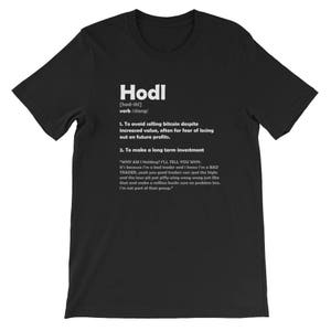May include: Black t-shirt with white text defining the slang term "Hodl" as a verb meaning to avoid selling bitcoin despite increased value, often for fear of losing out on future profits. The text also includes a definition of the term as a long-term investment strategy.