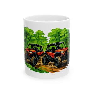 Könnte beinhalten: Ein weißer Keramikbecher mit einer farbenfrohen grafischen Illustration von zwei orangefarbenen Geländefahrzeugen, die auf einem schlammigen Waldweg zwischen grünen Bäumen fahren. Das Motiv erstreckt sich über die Außenseite des Bechers.