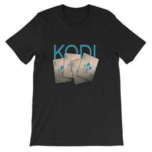 Peut inclure: T-shirt noir avec le mot "KODI" en texte bleu et quatre cartes à jouer avec l'as de pique en bleu sur chaque carte.
