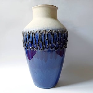 May include: A blue and white ceramic vase with a textured black rim. The vase has a gradient of blue and white glaze.
