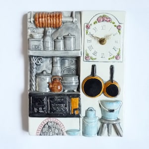 May include: A white ceramic wall plaque depicting a vintage kitchen scene. The plaque features a clock, a stove, a shelf with various kitchen utensils, and a hanging pot and pan. The plaque is decorated with floral accents and has a rustic charm.