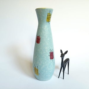 Könnte beinhalten: Eine hellblaue Keramikvase mit einem geometrischen Muster in Gelb, Rot und Schwarz. Die Vase ist hoch und schlank, mit einem abgerundeten Boden und einer schmalen Öffnung.