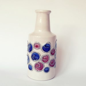 Puede incluir: Jarrón de cerámica blanca con un patrón geométrico de círculos azules y rosas. El jarrón tiene un cuello estrecho y una base ancha.