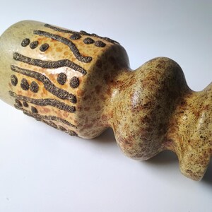 Puede incluir: Un jarrón de cerámica con una forma única y superficie texturizada. El jarrón presenta una combinación de colores beige y marrón con patrones lineales y punteados de color marrón oscuro. El jarrón tiene un cuerpo bulboso y una abertura acampanada.