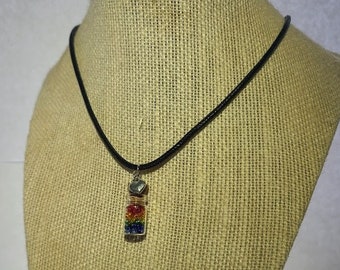 May include: A necklace with a black cord and a small glass vial pendant. The vial is filled with colorful beads arranged in a rainbow pattern. A small silver heart charm is attached to the top of the vial. The necklace is displayed on a mannequin.
