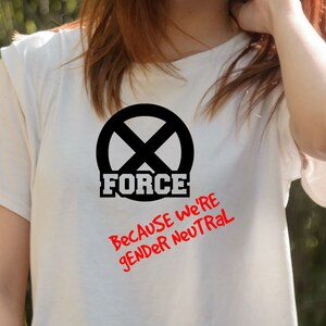Puede incluir: Camiseta blanca con un c&iacute;rculo negro que contiene una 'X' y la palabra 'FORCE' en letras negras. Debajo del c&iacute;rculo est&aacute; el texto 'Because we're gender neutral' en rojo.