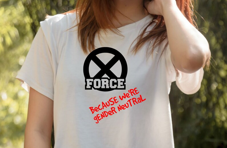 Puede incluir: Camiseta blanca con un c&iacute;rculo negro que contiene una 'X' y la palabra 'FORCE' en letras negras. Debajo del c&iacute;rculo est&aacute; el texto 'Because we're gender neutral' en rojo.