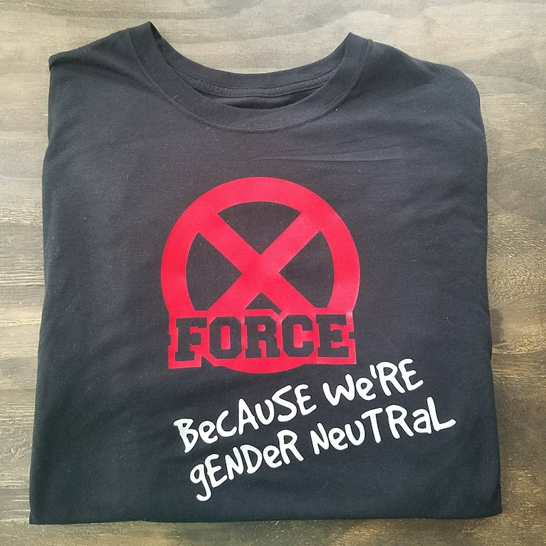 Puede incluir: Camiseta negra con un c&iacute;rculo rojo y una l&iacute;nea diagonal que lo atraviesa. La palabra "FORCE" est&aacute; escrita en letras negras debajo del c&iacute;rculo. El texto "BECAUSE WE'RE GENDER NEUTRAL" est&aacute; escrito en blanco debajo de la palabra "FORCE".