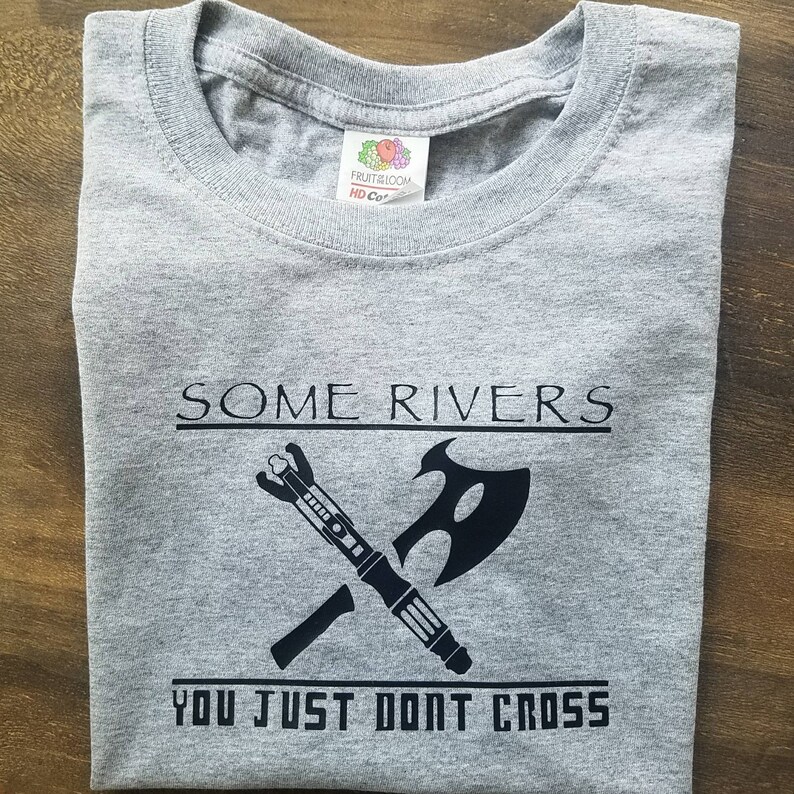 May include: Gray t-shirt with the text "SOME RIVERS YOU JUST DONT CROSS" in black. The shirt features a crossed graphic of a futuristic weapon and an axe.