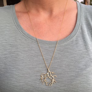 May include: A gold necklace with a delicate branch-shaped pendant. The pendant is made of thin, intricate metalwork and resembles a tree branch.