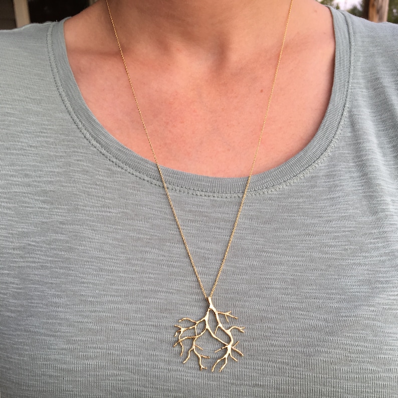 May include: A gold necklace with a delicate branch-shaped pendant. The pendant is made of thin, intricate metalwork and resembles a tree branch.