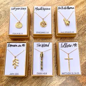 May include: Six small boxes with gold necklaces inside. Each box has a different design and a bible verse. The boxes are on a wooden surface.