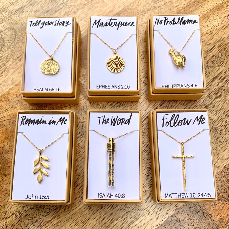 May include: Six small boxes with gold necklaces inside. Each box has a different design and a bible verse. The boxes are on a wooden surface.