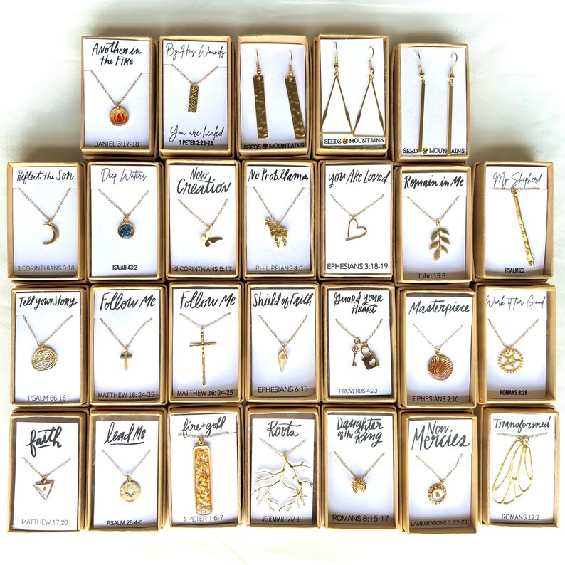 May include: A collection of 20 gold necklaces and earrings with various religious and inspirational quotes and scripture verses. Each piece is displayed in a small box with a white background and black text.