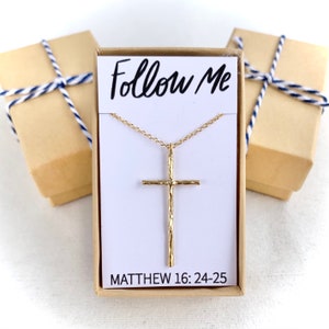 May include: A gold necklace with a textured cross pendant and a chain. The necklace is in a white box with the words "Follow Me" and "Matthew 16:24-25" printed on it.