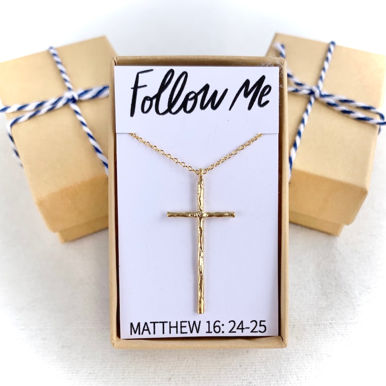 May include: A gold necklace with a textured cross pendant and a chain. The necklace is in a white box with the words "Follow Me" and "Matthew 16:24-25" printed on it.