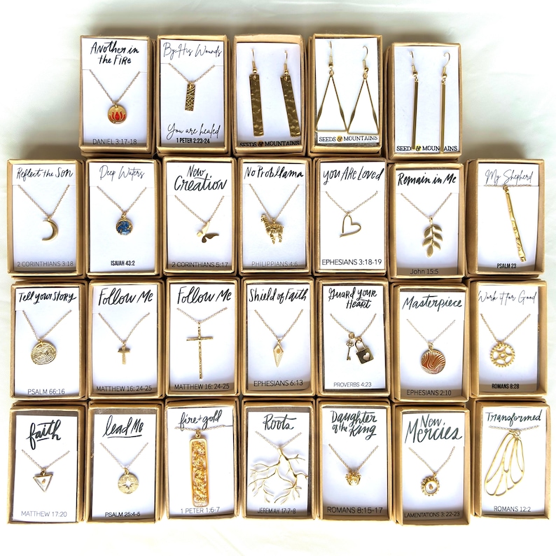May include: A collection of 20 gold necklaces and earrings with various religious and inspirational quotes and scripture verses. Each piece is displayed in a small box with a white background and black text.