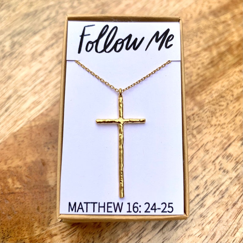 May include: Gold necklace with a hammered cross pendant and a chain. The pendant has the words "Follow Me" and "Matthew 16:24-25" on the box.