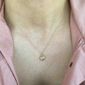 May include: A gold chain necklace with a small sun pendant. The pendant has a textured, circular design with a raised center.