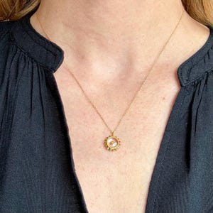May include: A gold chain necklace with a small, round pendant featuring a sun design with a clear glass center. The pendant is about the size of a dime.