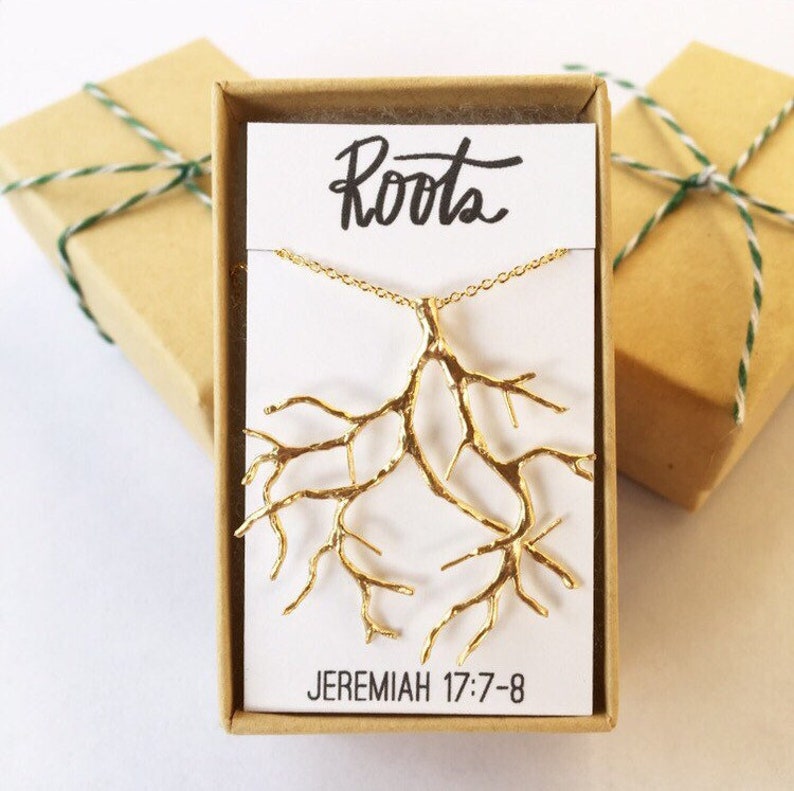May include: A gold necklace with a tree root pendant. The pendant is in the shape of a tree root with many branches. The necklace is in a small box with a white card that says "Roots" and "Jeremiah 17:7-8".