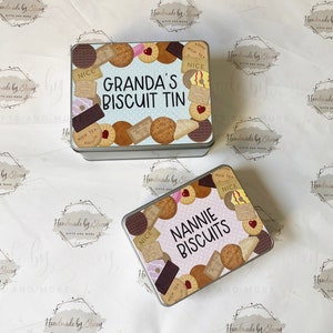 May include: Two metal biscuit tins with colorful designs. The top tin says "GRANDA'S BISCUIT TIN" and the bottom tin says "NANNIE BISCUITS". Both tins feature a variety of biscuits and the text "RICH TEA" and "NICE".