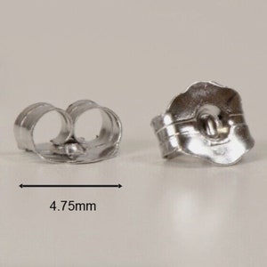 May include: Two silver earring backs, one with the back facing the viewer and the other with the front facing the viewer. The back is a simple loop, and the front has a small hole in the center. The earring backs are 4.75 mm wide.