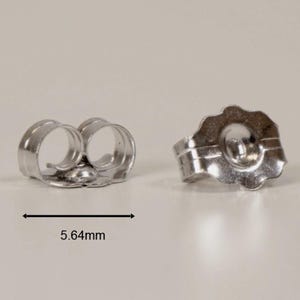 May include: Two silver-colored earring backs. One back has a scalloped edge and a circular indentation. The other back has two loops. The measurement of 5.64mm is indicated.