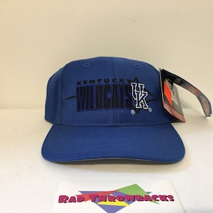 Peut inclure: Casquette de baseball bleue avec une étiquette blanche attachée. La casquette a un logo brodé noir et bleu qui dit "Kentucky Wildcats" avec un logo bleu "UK".