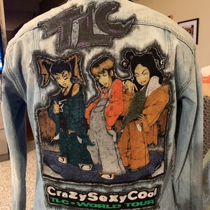 May include: A light blue denim jacket with a large embroidered patch featuring a cartoon image of three women with the text "Crazy Sexy Cool TLC World Tour".