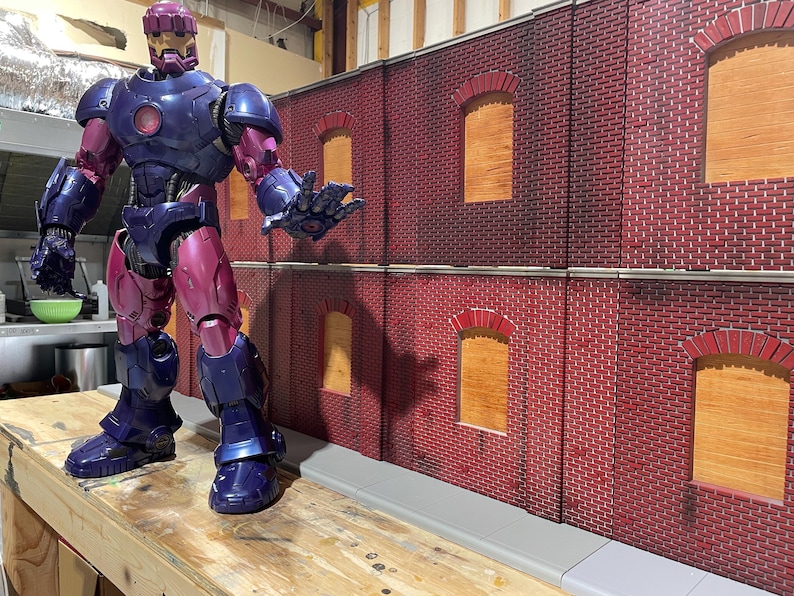 May include: A purple and silver action figure of a superhero standing in front of a red brick wall with boarded up windows. The figure has a helmet with a gold visor and a detailed suit.