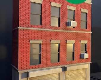 May include: A three-storey building model with a red brick facade, windows, and air conditioning units. The ground floor features two garage-style doors. The image includes a green circle with the words "FREE SHIPPING".