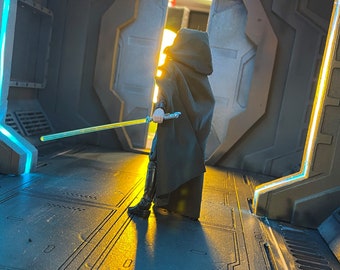 May include: A figure wearing a black hooded robe and holding a lightsaber stands in a futuristic hallway with blue and yellow lights. The figure is facing away from the camera and walking towards a doorway.