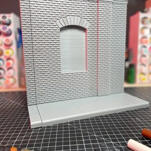 May include: A gray brick wall with a window and a sidewalk. The wall is made of small bricks and has a rough texture. The window is arched and has a white frame. The sidewalk is made of concrete and has a smooth surface.