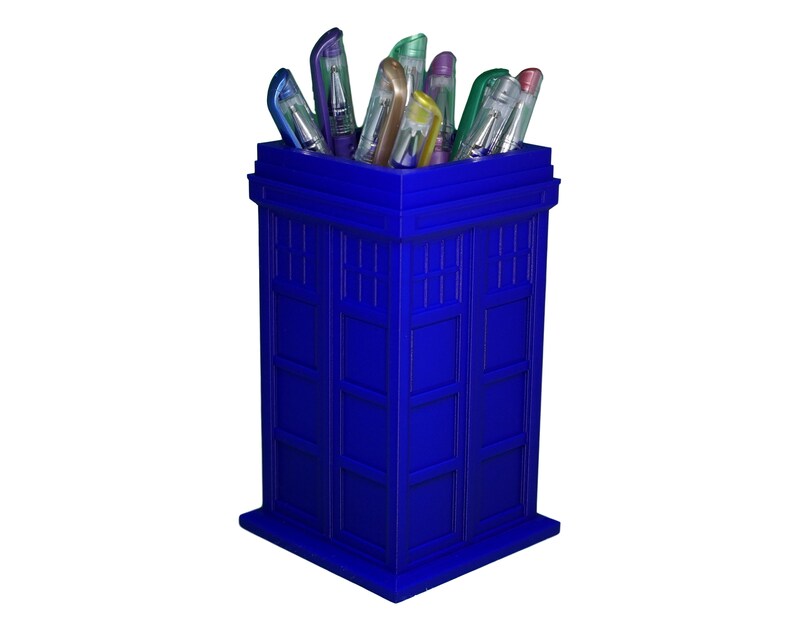 May include: A blue TARDIS-shaped desk organizer with a variety of colorful pens sticking out of the top.