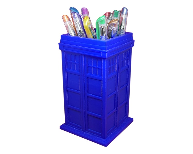 The stationery holder is designed to resemble the iconic police telephone box from the popular television show Doctor Who. It features a blue exterior with a rectangular shape and a flat top, adorned with a series of vertical panels that evoke the classic design of the TARDIS. The holder is made of PLA plastic, giving it a sturdy yet lightweight feel. It is filled with an assortment of colorful pens and pencils, adding a pop of vibrancy to the overall design.
