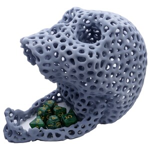 May include: A gray, 3D printed skull-shaped dice tower with a lattice design. Green dice with gold numbers are inside the tower.