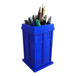 May include: A blue TARDIS-shaped desk organizer with a variety of pens and pencils inside.