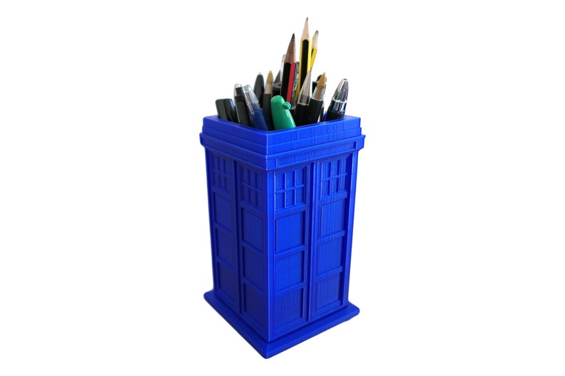 May include: A blue TARDIS-shaped desk organizer with a variety of pens and pencils inside.