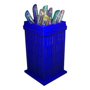 May include: A blue TARDIS-shaped pencil holder with colorful pens sticking out of the top.