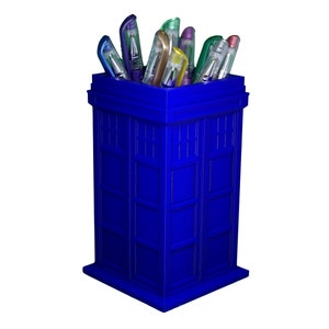 May include: A blue TARDIS-shaped pencil holder with a variety of colorful pens inside.
