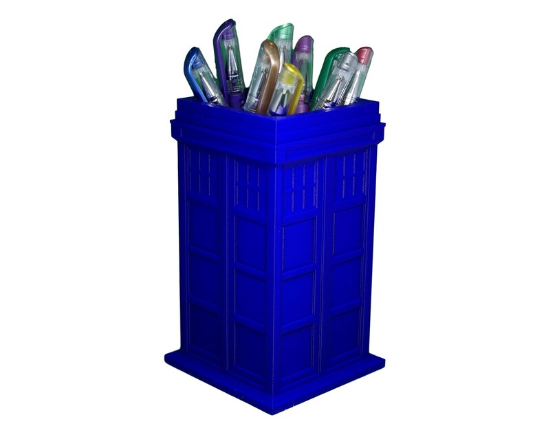May include: A blue TARDIS-shaped pencil holder with a variety of colorful pens inside.